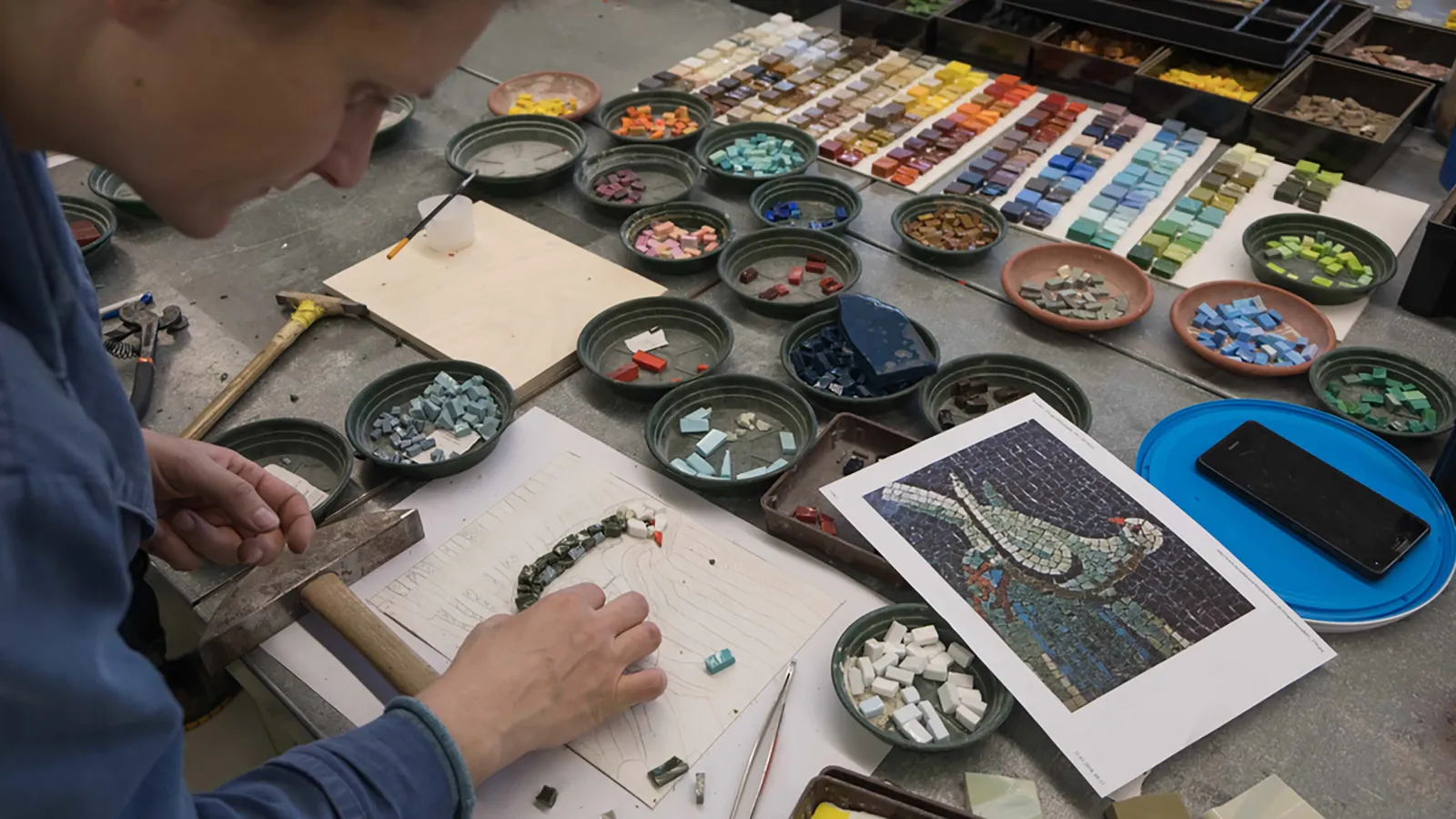 Eine Studentin legt ein Mosaik einer Taube mit bunten Mosaiksteinen