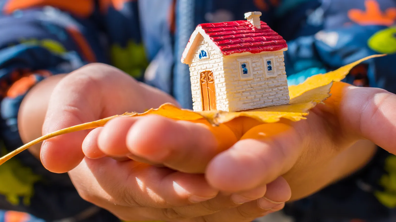 Zwei übereinander gelegte Kinderhände präsentieren ein Modellhaus