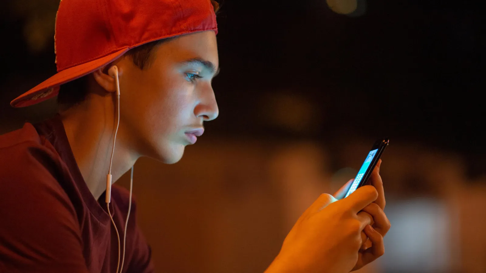 Junger Mann mit roter Basecap schaut auf sein Smartphone.