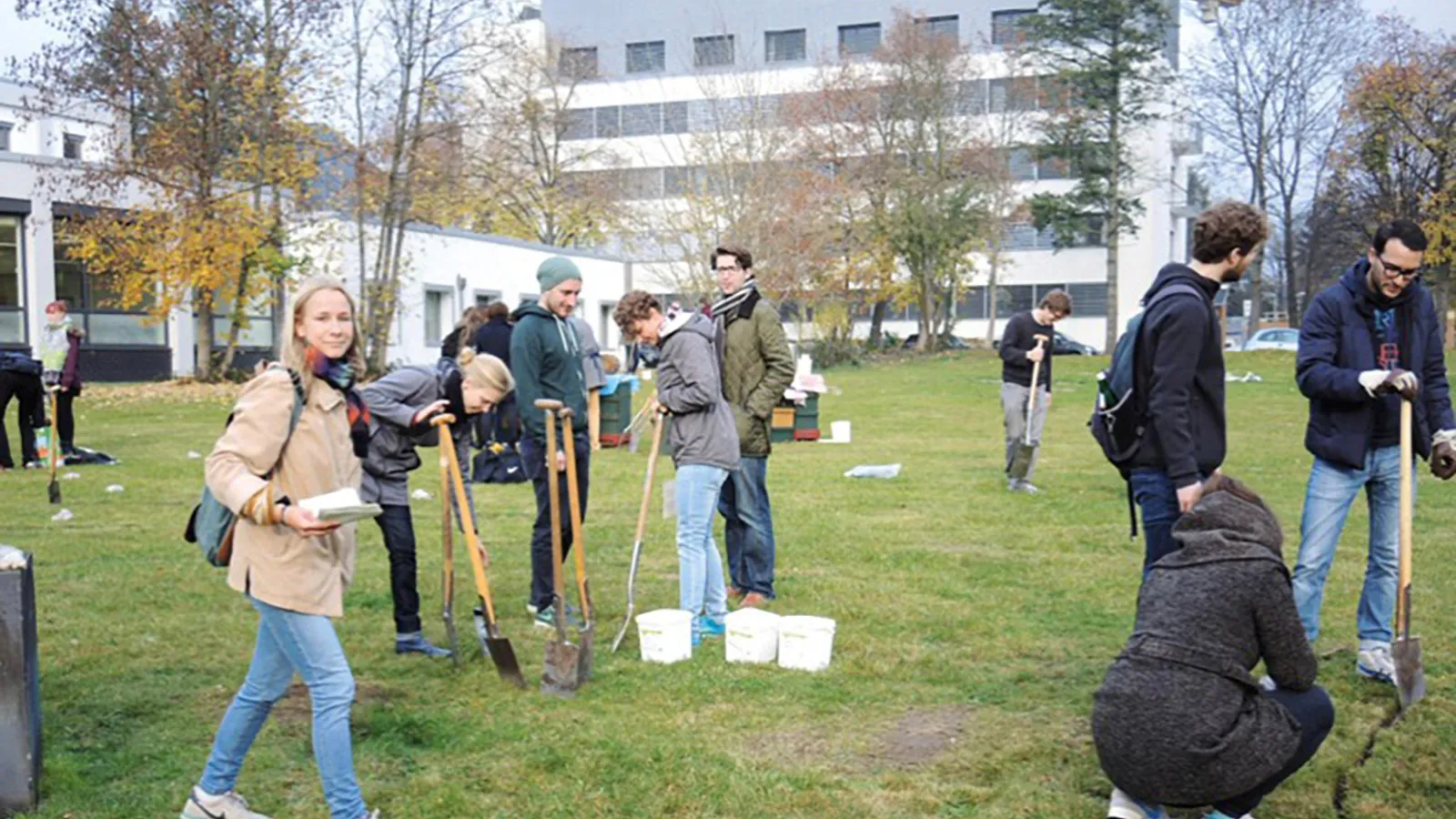 Teilnehmer*innen draußen auf einer Wiese mit Spaten