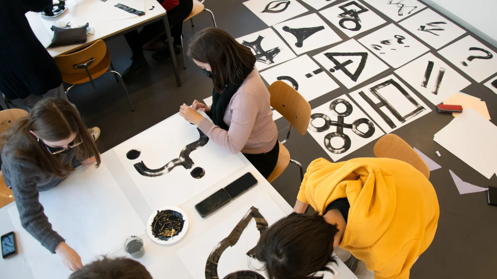 Die mit Pinsel auf DinA4 Blatt in schwarz gezeichneten Symbole der Teilnehmenden von oben fotografiert