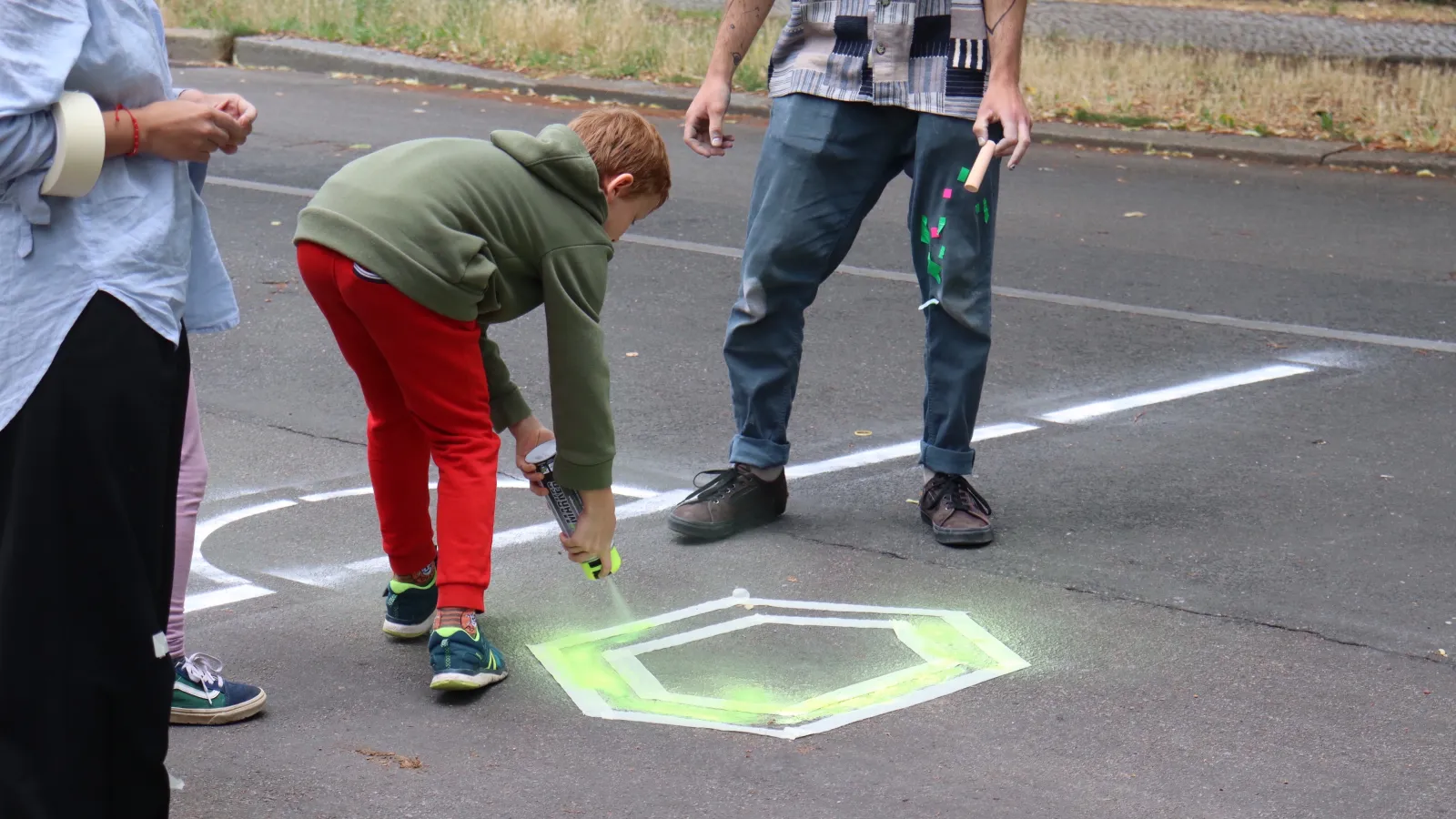 Teilnehmer sprüht in neongrün ein Pentagon auf den Asphaltboden