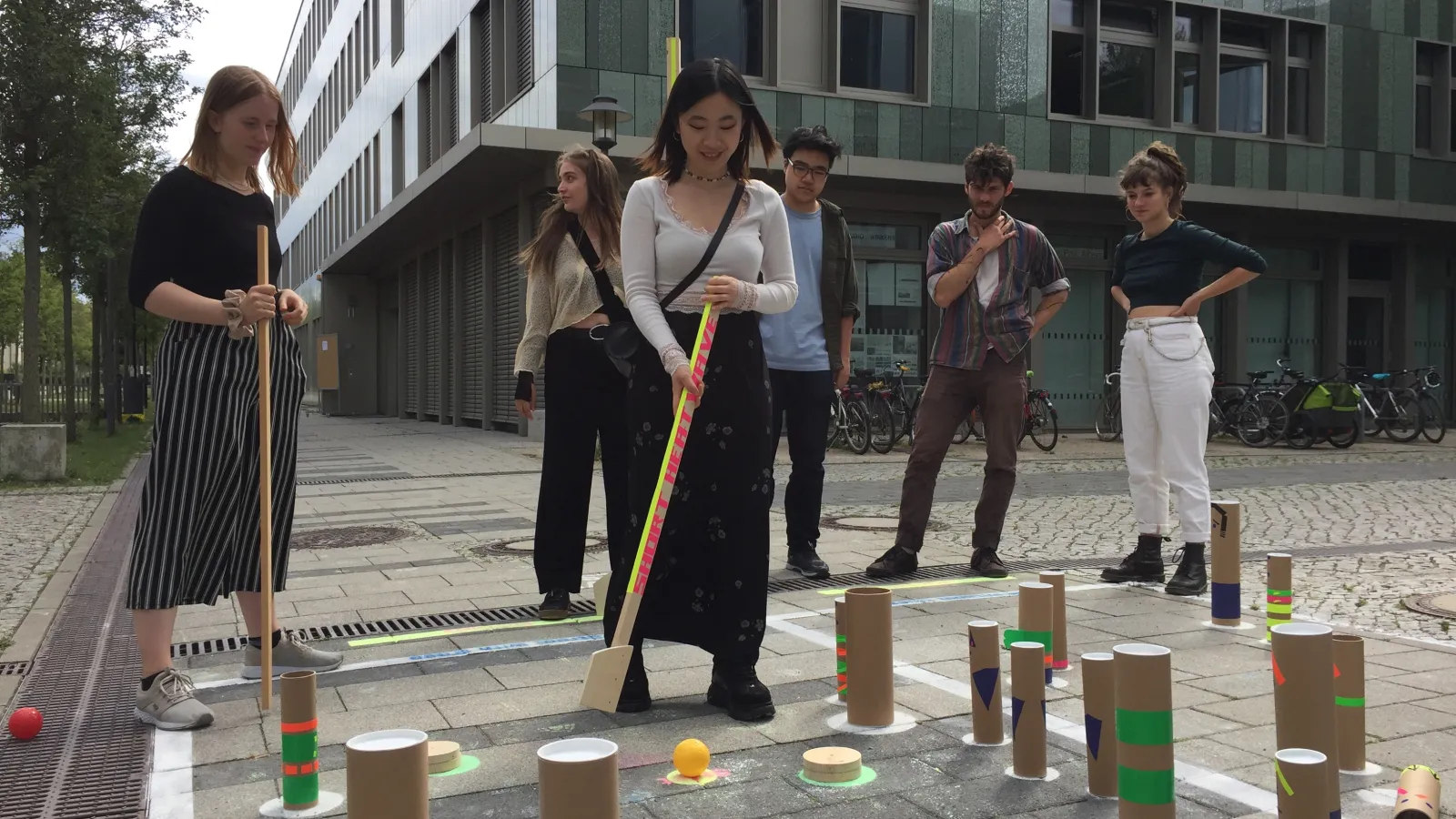 Teilnehmende spielen auf Asphaltboden ein dem Cricket ähnliches Spiel