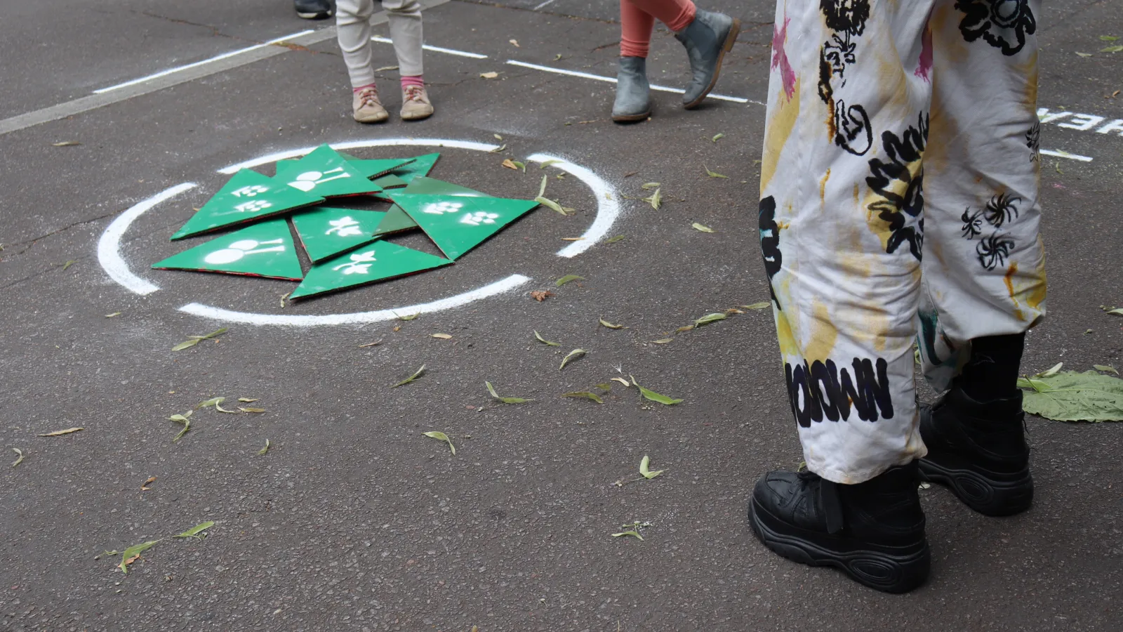 Grüne Papierdreiecke liegen auf dem Asphaltboden innerhalb eines gesprühten Kreises