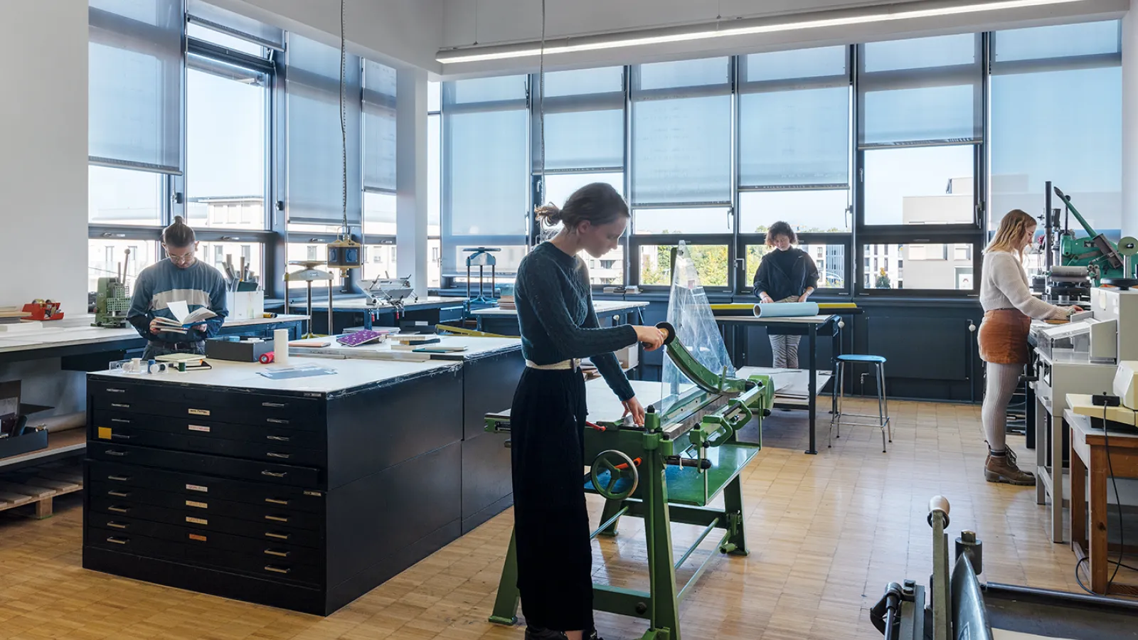 Blick in die Buchbindewerkstatt. Es arbeiten 3 Studierende an ihren Projekten.