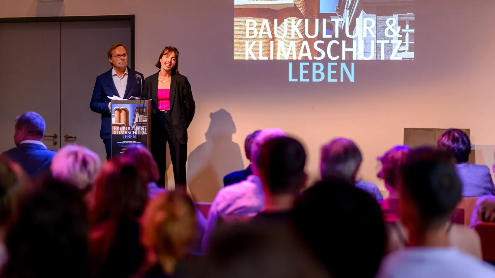 Hannah Hoepffner und Rudolf Spindler begrüßen auf der Bühne das Publikum zur 3. Veranstaltung der Reihe Baukultur und Klimaschutz leben