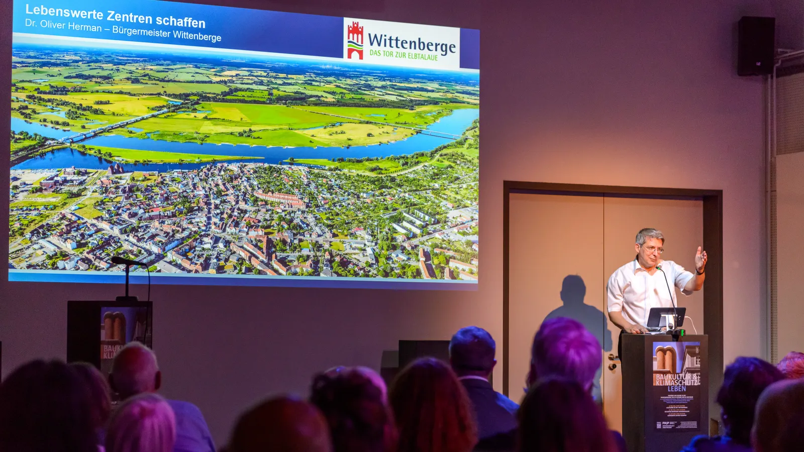 Dr. Oliver Hermann, Bürgermeister der Stadt Wittenberge (Prignitz), hält seinen Vortrag zum Thema "Lebenswerte Zentren schaffen in der Stadt Wittenberge" vor vielen interessierten Besucher*innen der 3. Veranstaltung der Reihe Baukultur und Klimaschutz leben