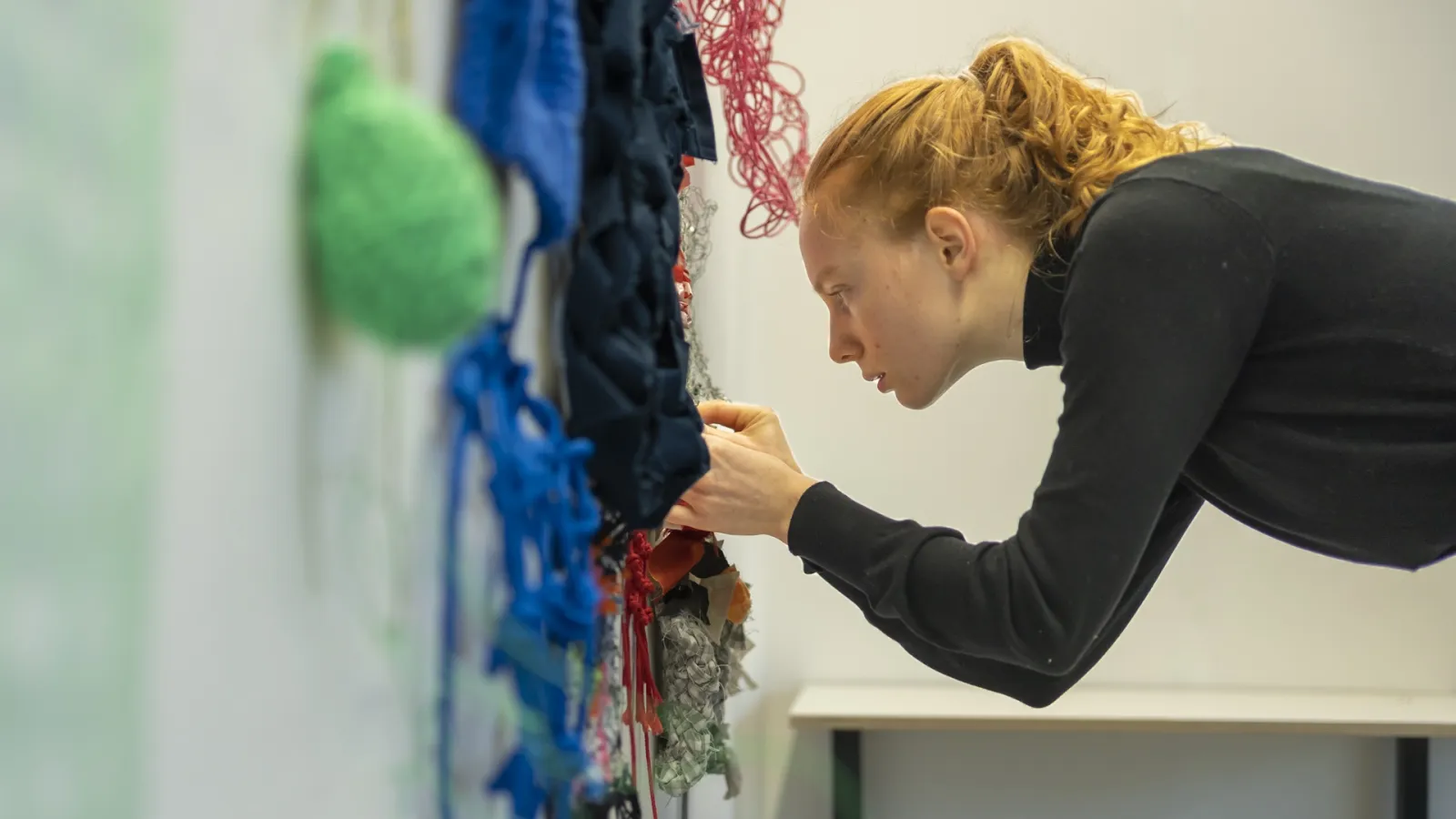 eine Person arbeitet an einer Textilarbeit an der Wand