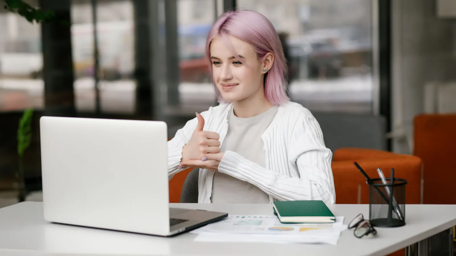 Junge gehörlose Frau hat eine digitale virtuelle Online-Konferenz am Computer, benutzt Gebärdensprache und zeigt Gesten am Bildschirm