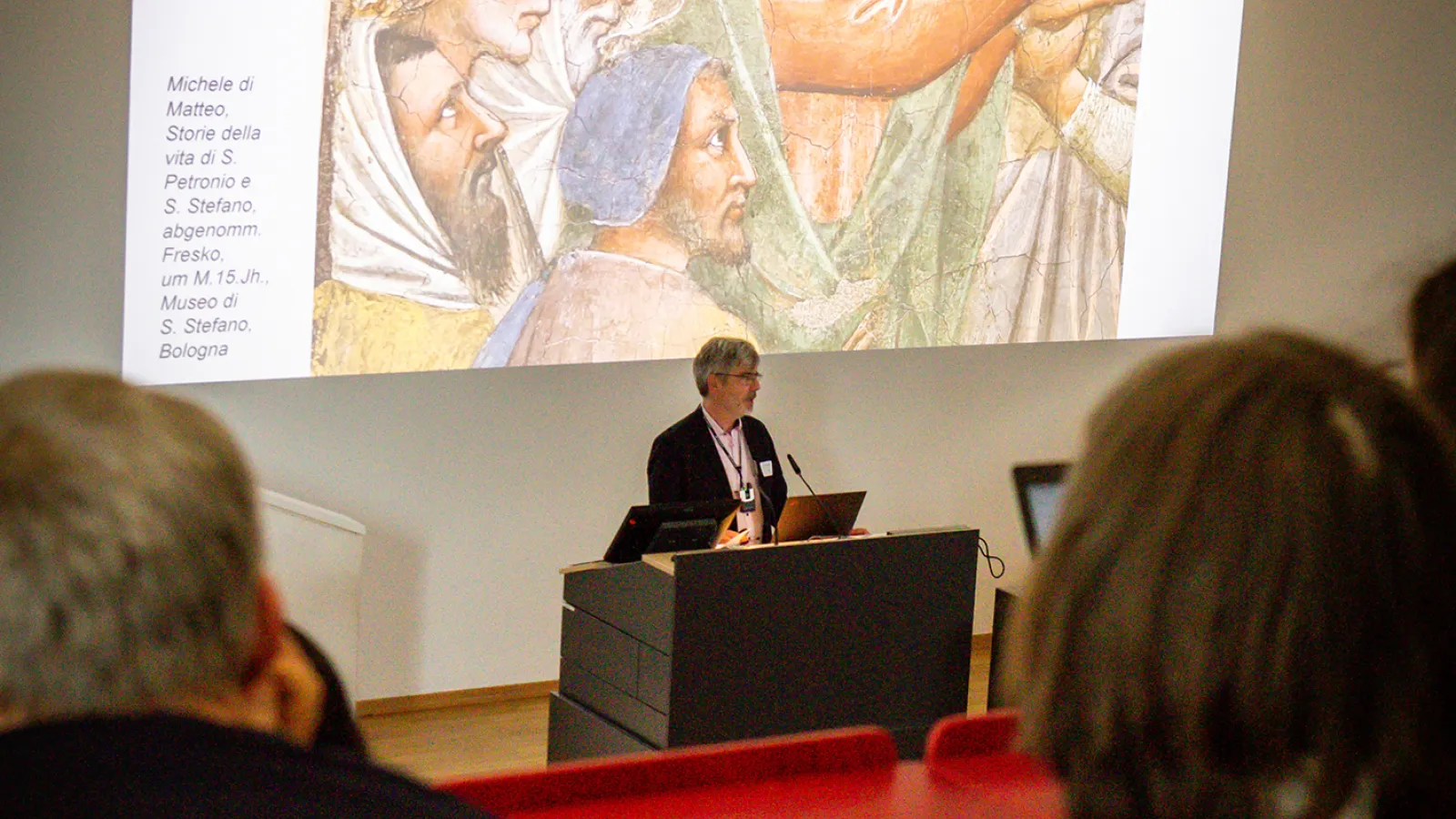 Prof. Dr. Jan Raue steht am Rednerpult, während ein Bild an die Wand projiziert wird.