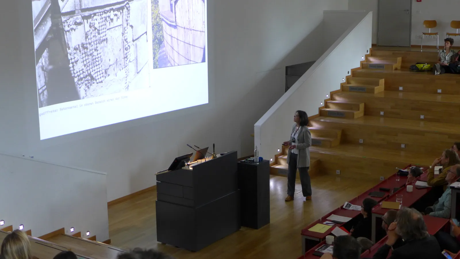 Frau Dr. Ute Joksch hält einen Vortrag im Hörsaal, während Zuhörende interessiert auf das projizierte Bild an der Wand schauen