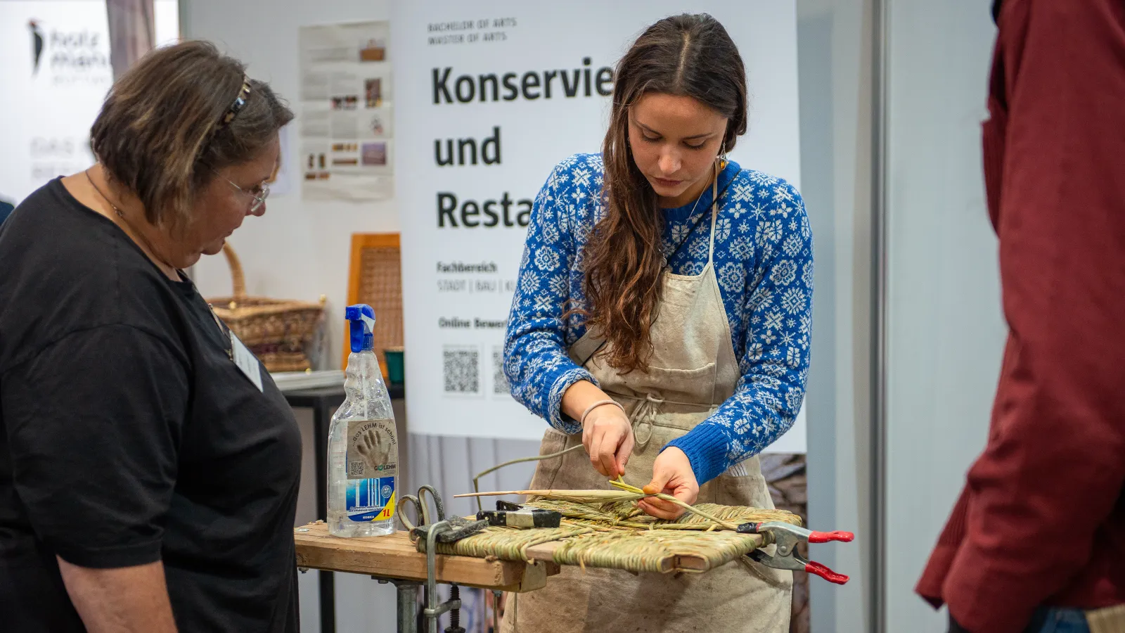 Die Masterstudentin Karoline Jüttner des Studiengangs Konservierung und Restaurierung demonstriert das Handwerk des Stuhlflechtens auf der denkmal 2024