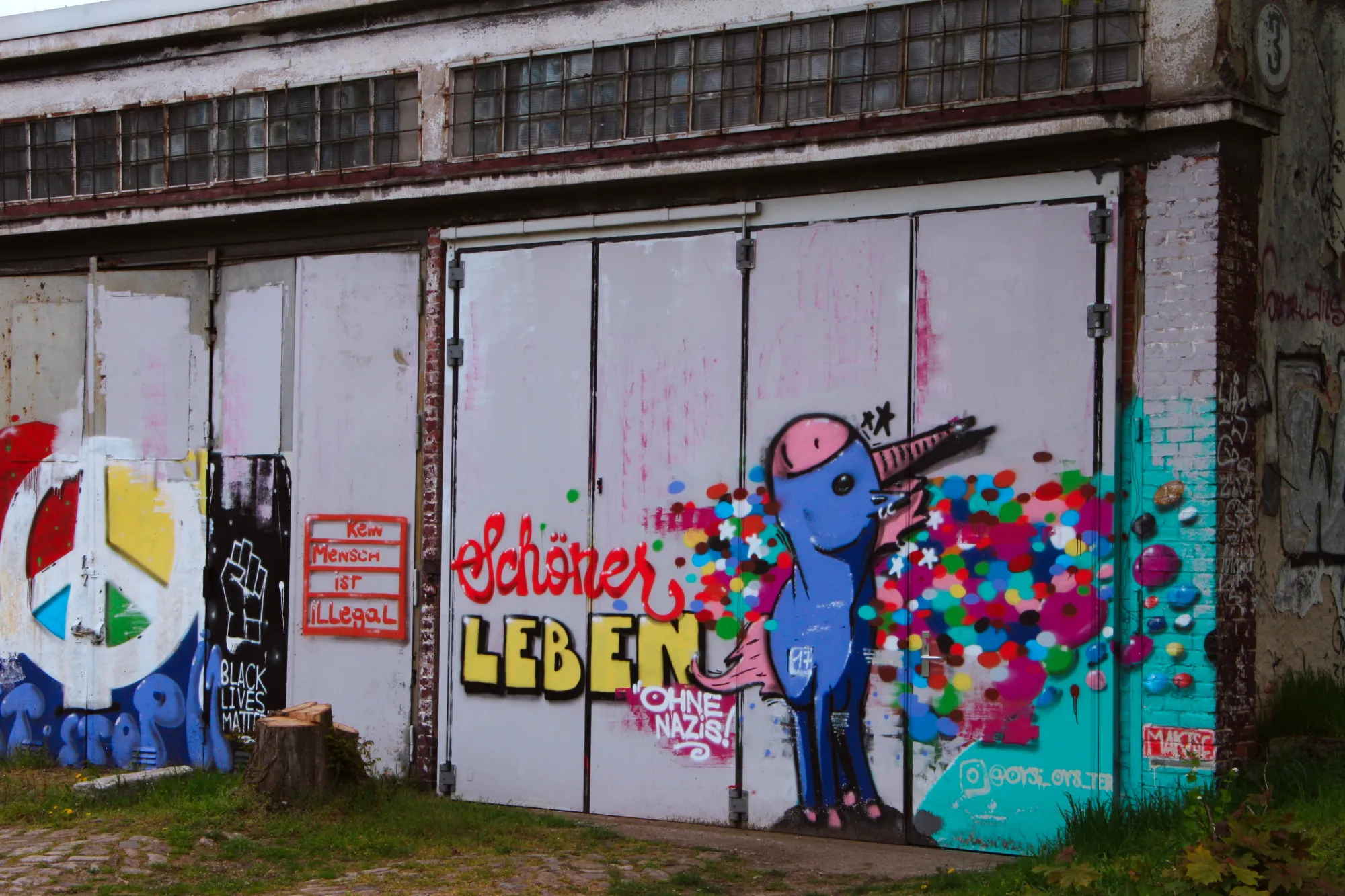 Graffiti auf der Panzerhalle mit Einhorn und Aufschrift "Schöner leben ohne Nazis" und großem Peace-Zeichen