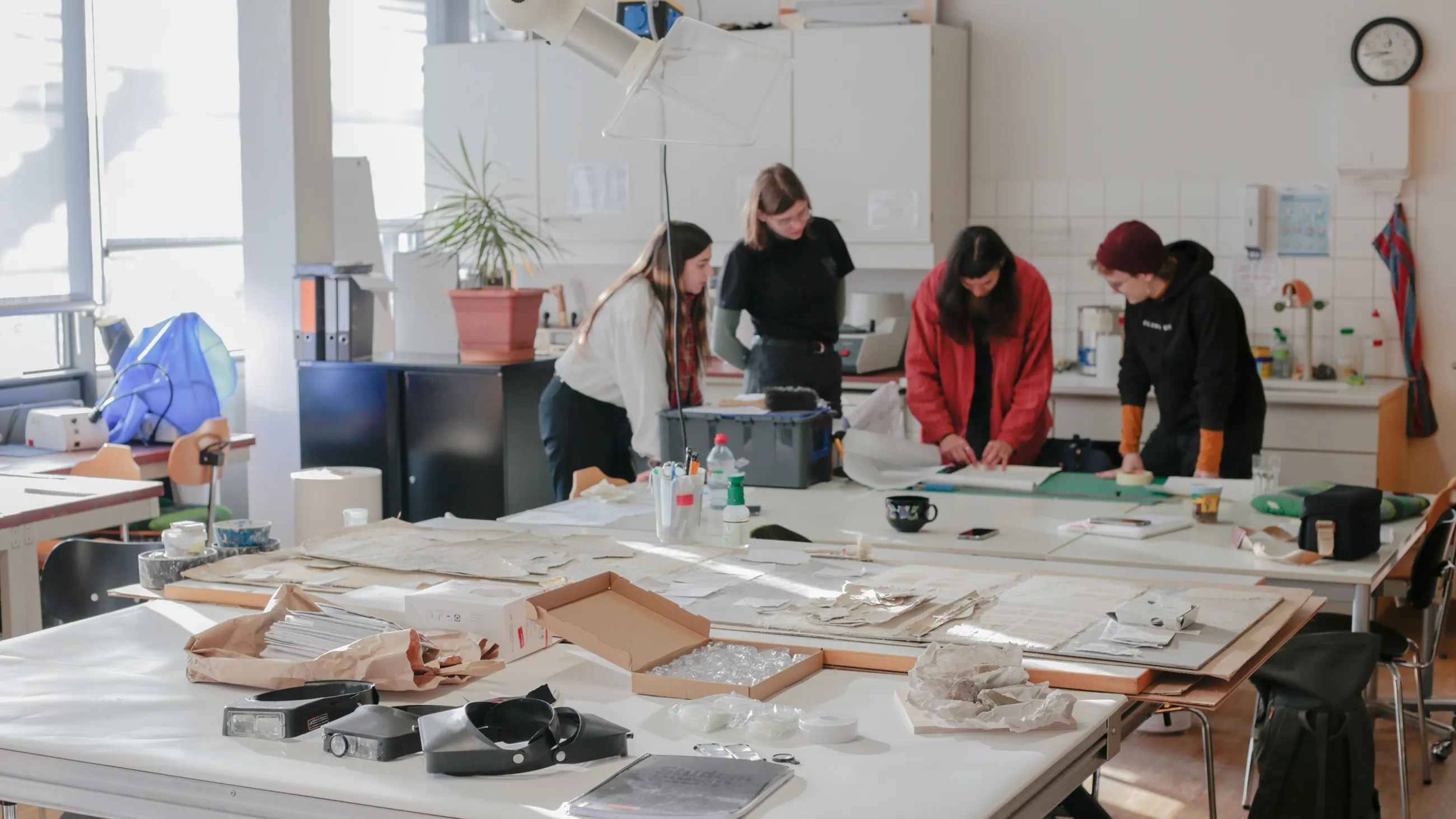 Vier Studierende stehen in der Werkstatt der Wandmalerei an einem Tisch