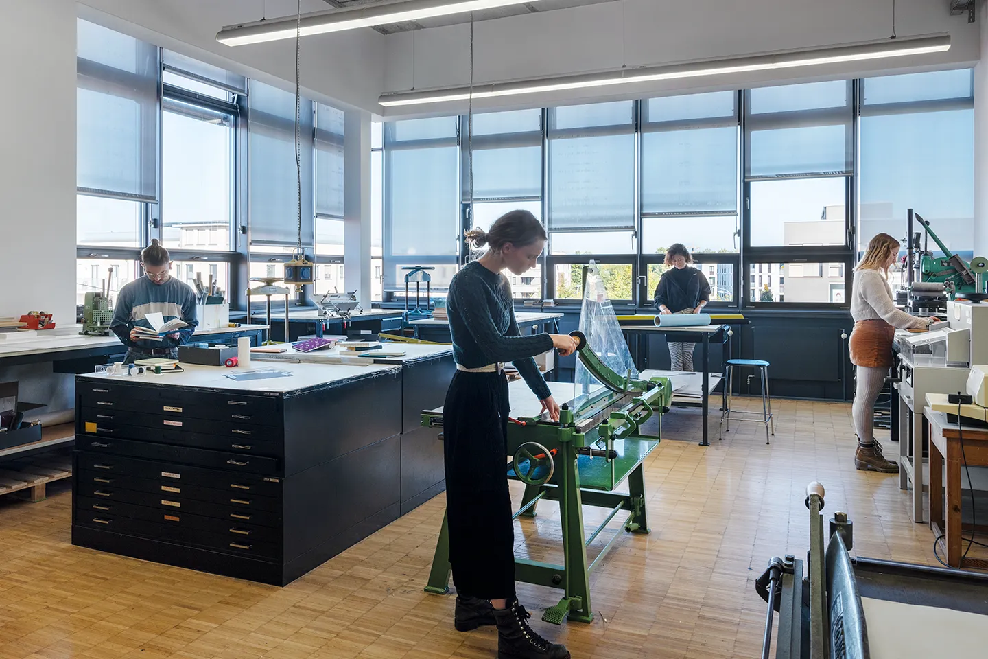 Blick in die Buchbindewerkstatt. Es arbeiten 3 Studierende an ihren Projekten.