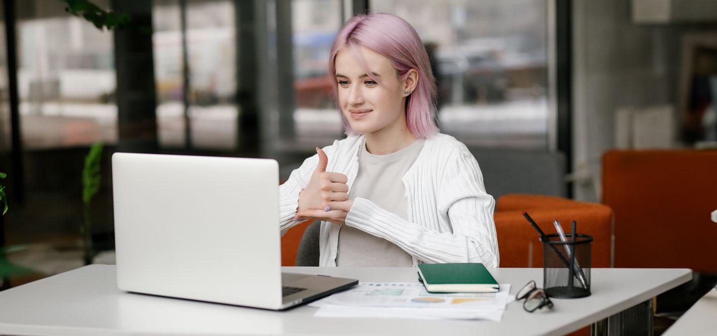 Junge gehörlose Frau hat eine digitale virtuelle Online-Konferenz am Computer, benutzt Gebärdensprache und zeigt Gesten am Bildschirm