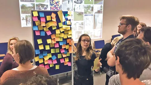 Studierende halten eine Präsentation vor einer Wand mit bunten Zetteln