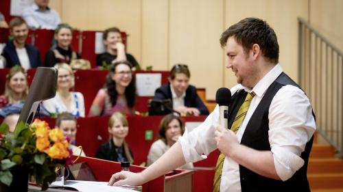 Ein Absolvent hält eine Rede vor einem vollen Hörsaal.